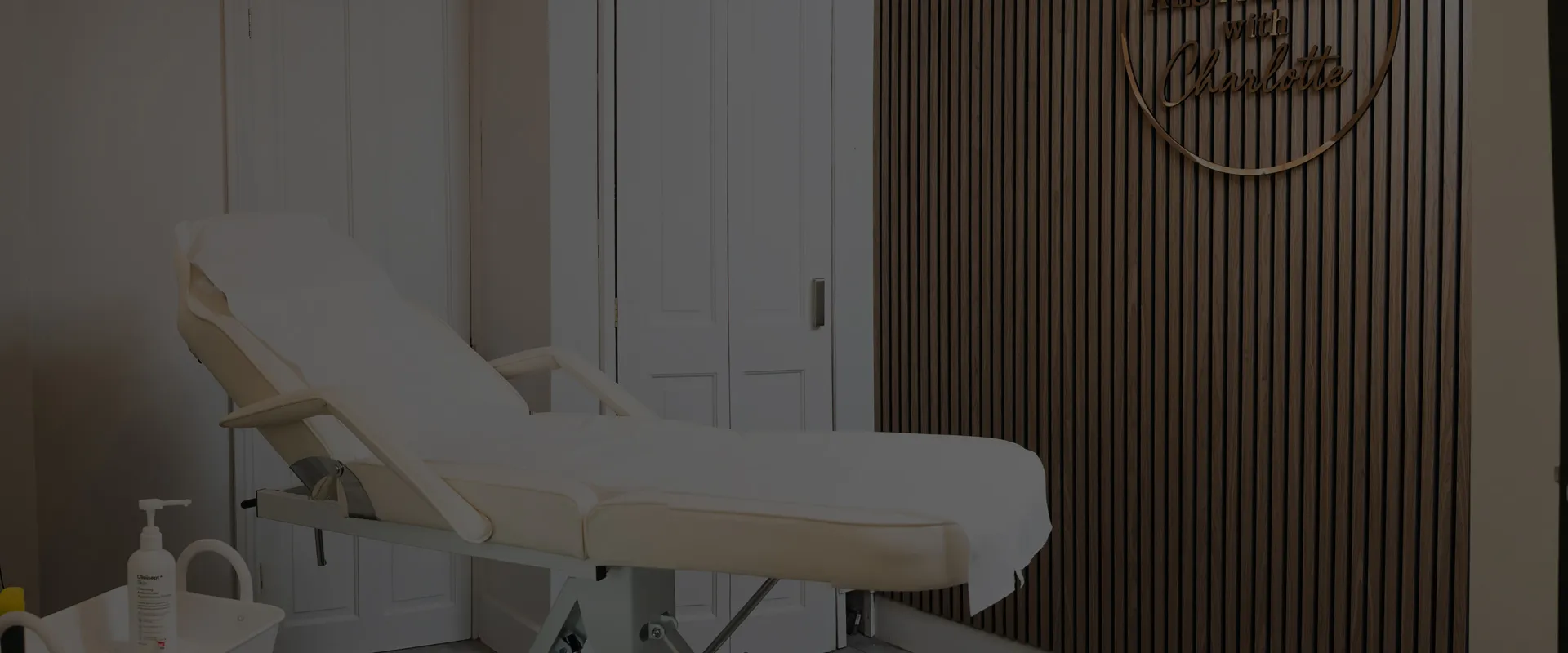 The treatment room at Aesthetics With Charlotte, the couch beside the slatted wall and her sign