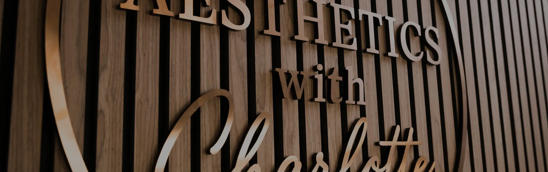 The Aesthetics With Charlotte sign in gold letters on the slatted wood wall of the clinic